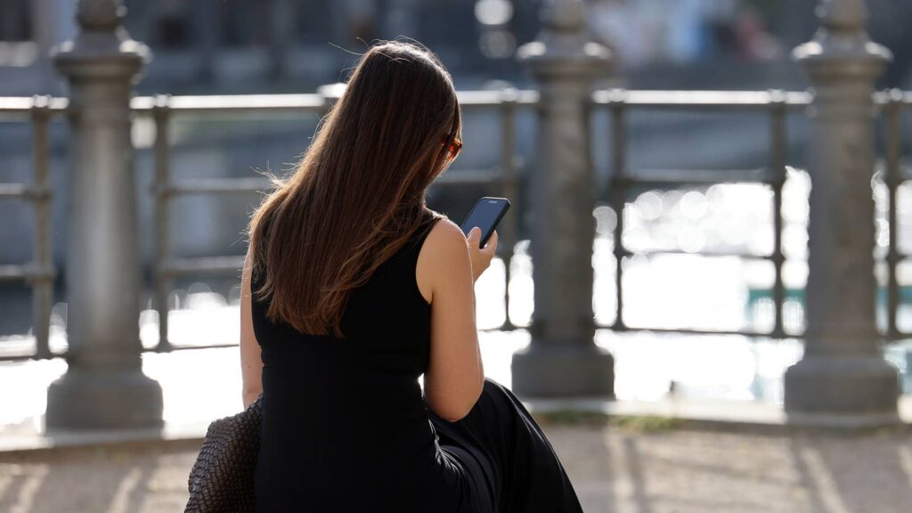 Iranian woman living abroad checking her phone while sitting by the riverside in Germany