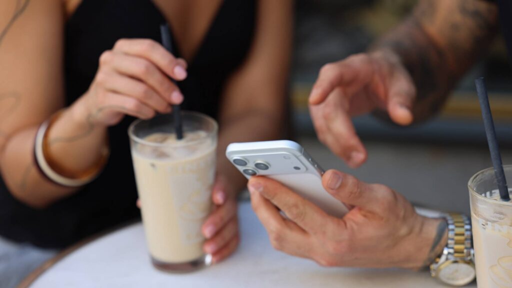 Two people meeting over coffee while looking at a smartphone together.