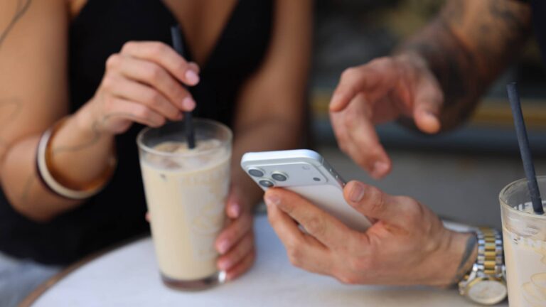 Two people meeting over coffee while looking at a smartphone together.
