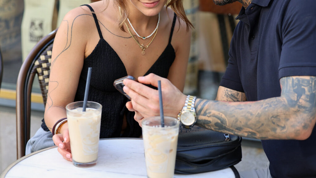 Couple sitting at a cafe table looking at a phone together